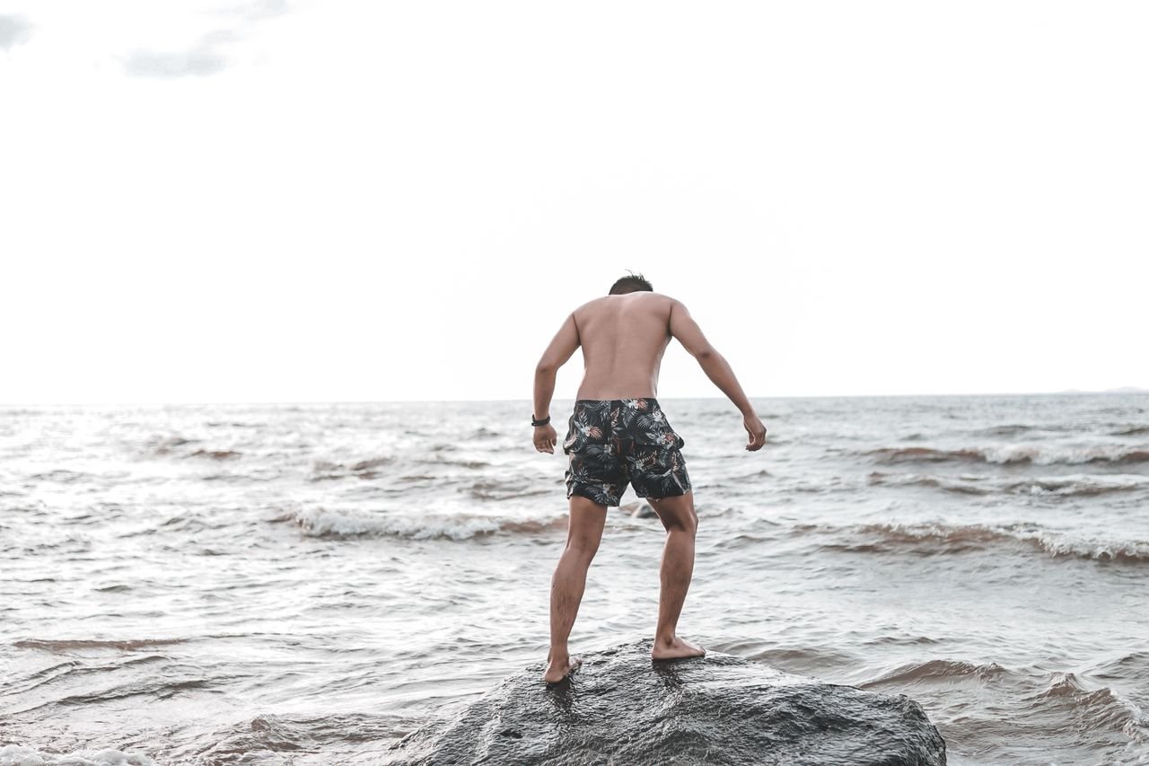 services-01 A young man stands on a rock by the sea, capturing a moment of summer adventure.