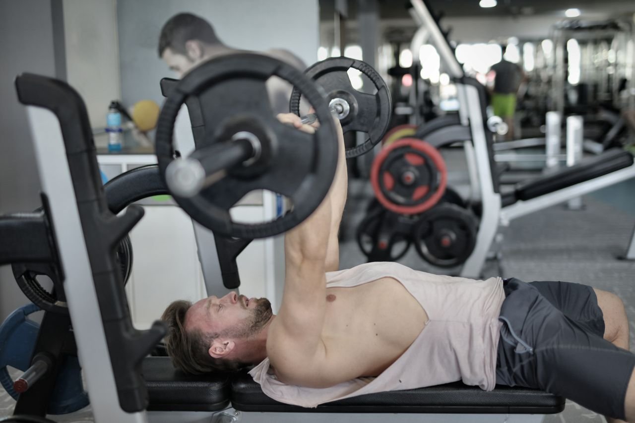 our-services-1 Side view of strong young sportsman in sportswear lying on bench and pressing heavy barbell doing chest exercise training in modern gym